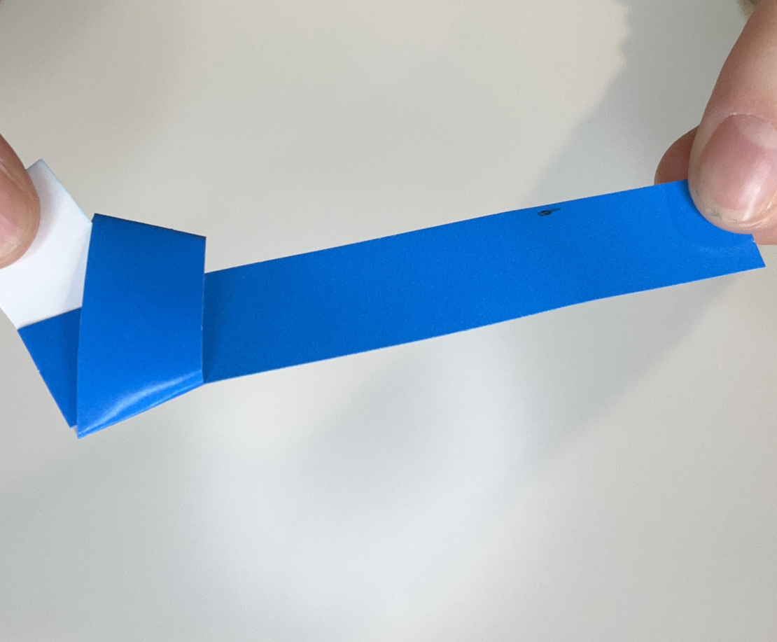 Knot of your blue paper strip being pulled tighter to create pentagon shape.